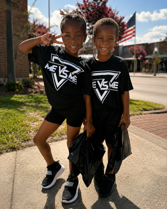 Two children wearing black t-shirts with a logo, standing on a sidewalk.